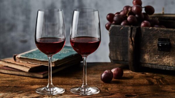 Foto mostra duas taças de vinho tinto em cima da mesa ao lado de um cacho de uvas.