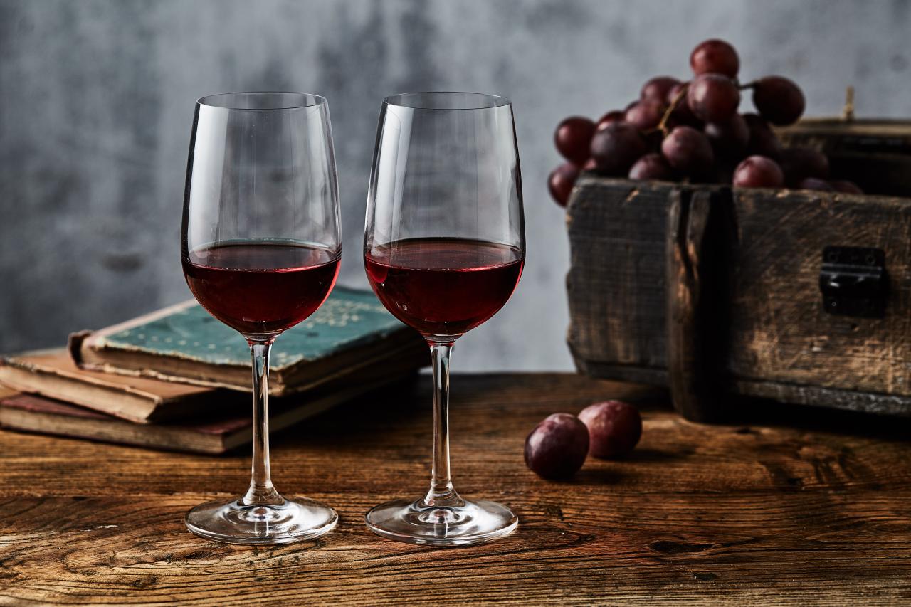 Foto mostra duas taças de vinho tinto em cima da mesa ao lado de um cacho de uvas.