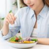 Foto mostra mulher comendo um cumbuca de legumes e frutas.