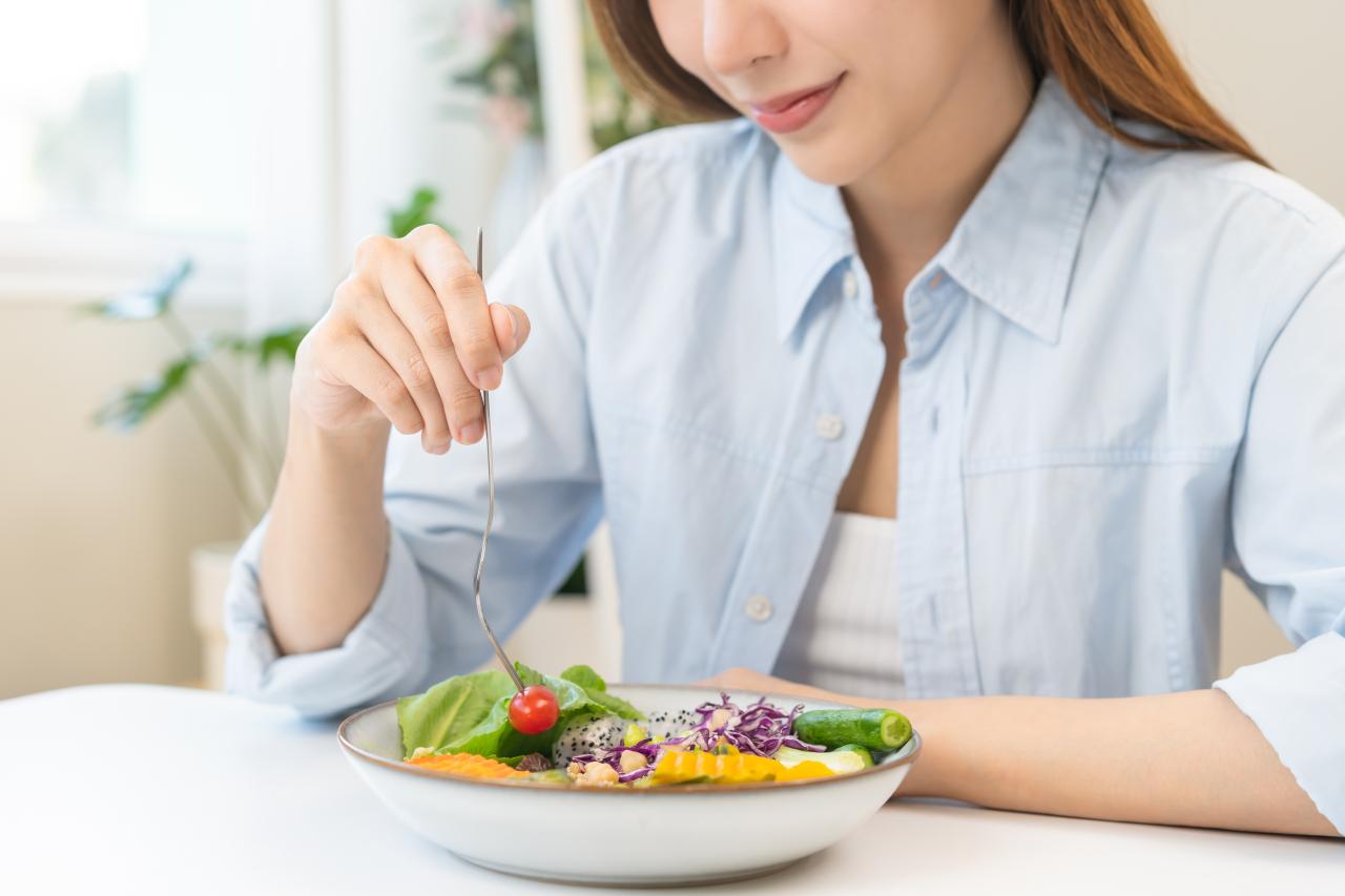 Foto mostra mulher comendo um cumbuca de legumes e frutas.