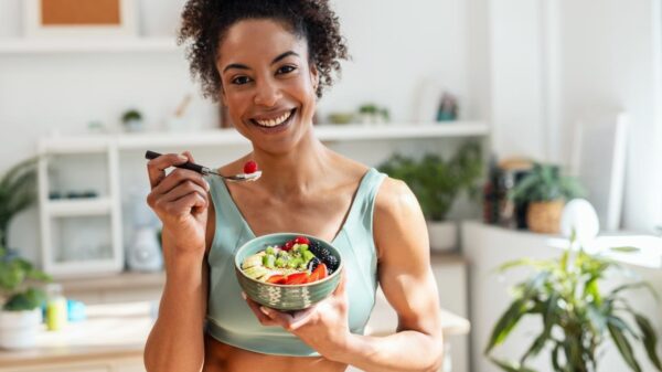 Mulher negra sorrindo segurando uma cumbuca com frutas e legumes.