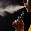 Foto mostra uma pessoa fumando vape enquanto sai fumaça.