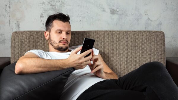 Homem sentado no sofá mexendo no celular.