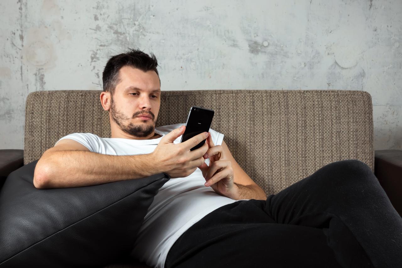 Homem sentado no sofá mexendo no celular.