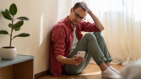 Imagem de um homem sentado no chão segurando o celular o olhando para a tela confuso