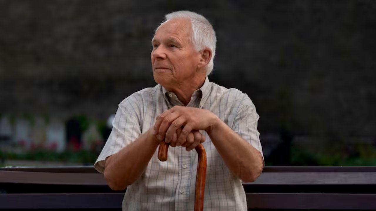 Imagem de um idoso sentado apoiado na bengala