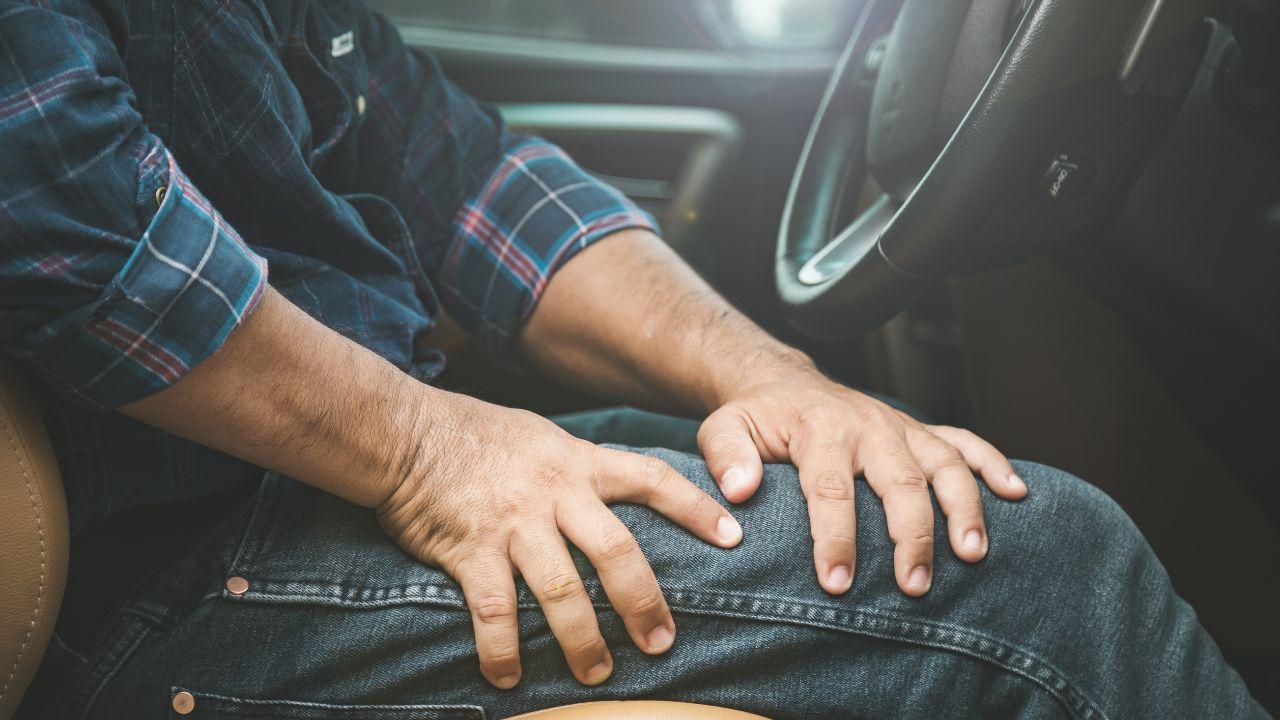 Imagem de um homem no banco do motorista de um carro com as mãos na perna