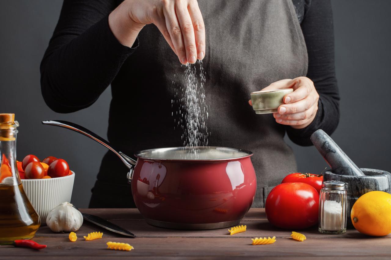 Foto mostra uma pessoa colocando sal dentro de uma panela com comida.