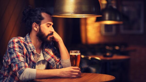 Foto mostra homem sentado em um bar bebendo uma taça de cerveja.