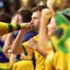 Torcedores com camisetas amarelas torcendo para o Brasil no estádio.
