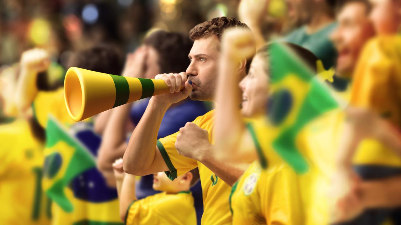 Torcedores com camisetas amarelas torcendo para o Brasil no estádio.