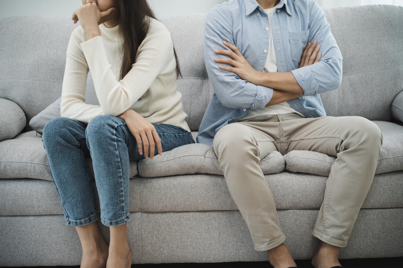 Homem e mulher sentados de costas um pro outro no sofá.