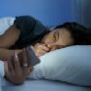 Mulher deitada na cama no escuro mexendo no celular.