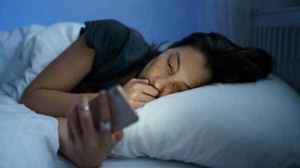 Mulher deitada na cama no escuro mexendo no celular.