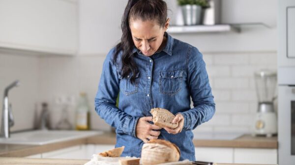 Imagem de uma mulher comendo uma fatia de pão com a mão na barriga e cara de dor