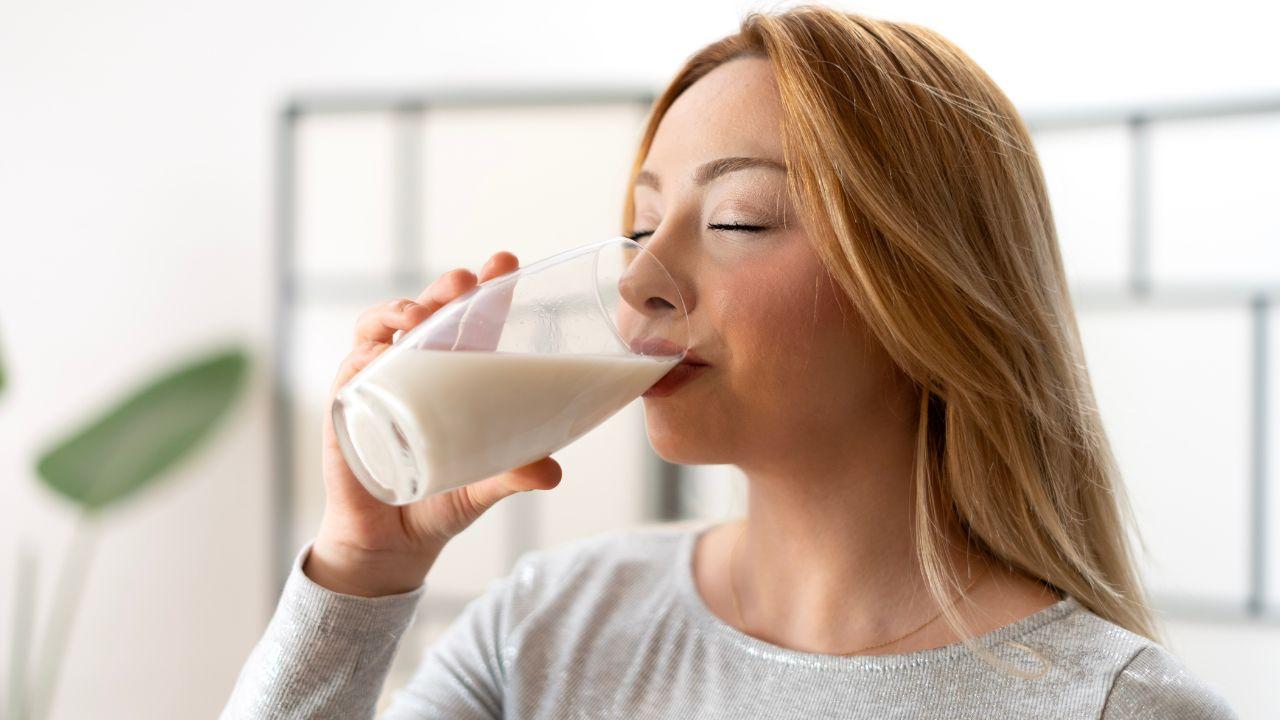 Imagem de uma mulher bebendo leite em um copo de vidro longo