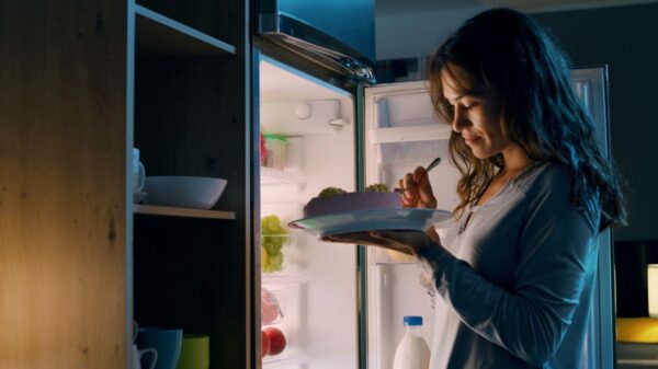 Imagem de uma mulher na frente da geladeira a noite comendo algo