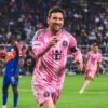 Imagem de Lionel Messi em campo com uniforme rosa apontando para frente comemorando