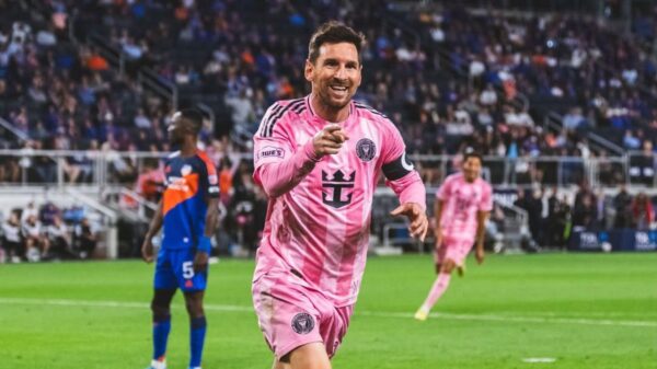 Imagem de Lionel Messi em campo com uniforme rosa apontando para frente comemorando