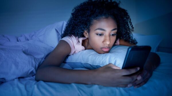 Mulher negra deitada na cama no escuro e mexendo no celular.