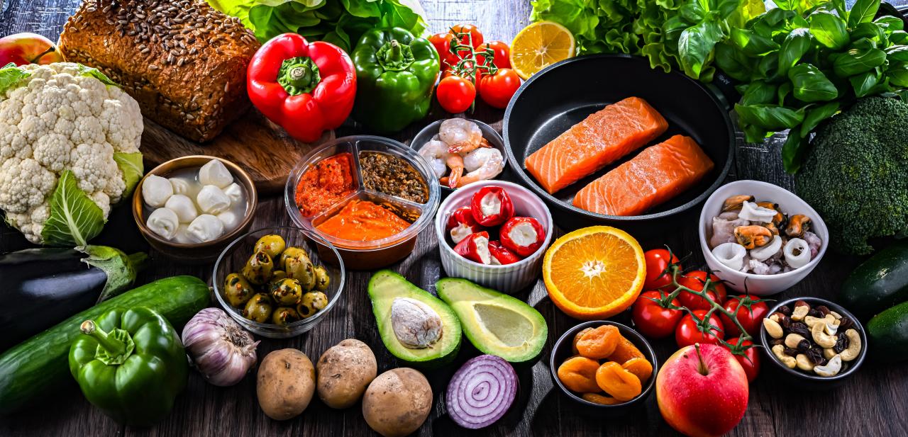 Vários alimentos reunidos em cima de uma mesa. Tem carnes, frutas e verduras.