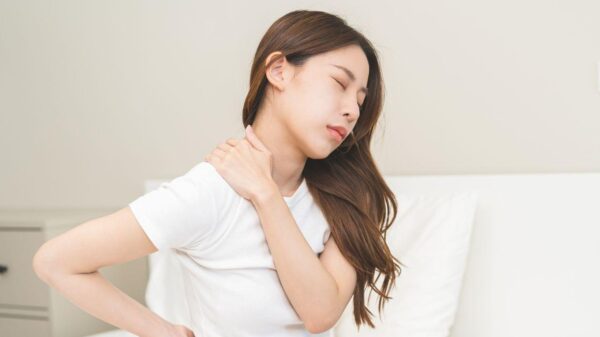 Imagem de uma mulher jovem com as mãos nas costas sentada na cama