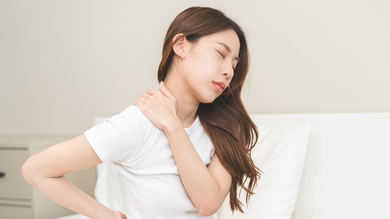 Imagem de uma mulher jovem com as mãos nas costas sentada na cama