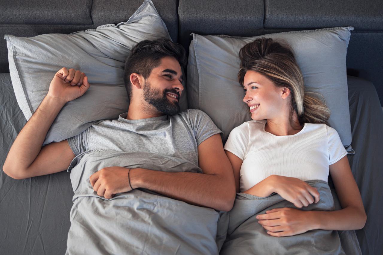 Mulher e homem deitados na cama sorrindo um para o outro.