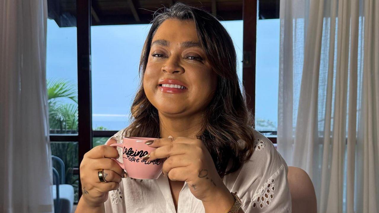 Foto mostra Preta Gil com blusa branca e tomando um chá sorrindo.