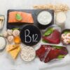 Foto mostra vários alimentos que tem B12 e um cartaz no meio escrito B12.