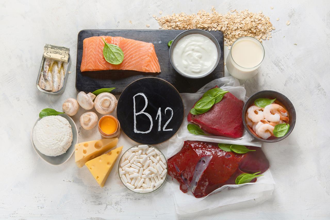 Foto mostra vários alimentos que tem B12 e um cartaz no meio escrito B12.