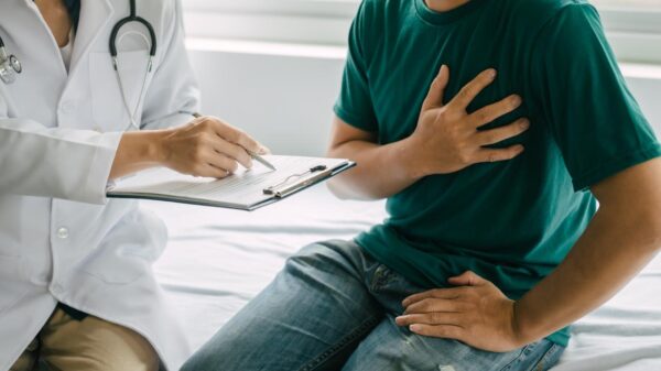 Foto mostra homem sentado no consultório com a mão no peito enquanto uma médica o consulta.
