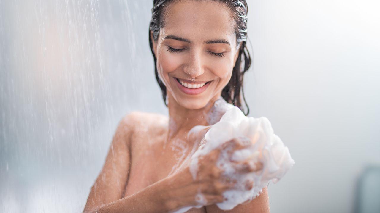 Imagem de uma mulher tomando banho com uma bucha cheia de espuma