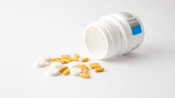 Imagem de um pote de medicamentos aberto e deitado na mesa com comprimidos espalhados