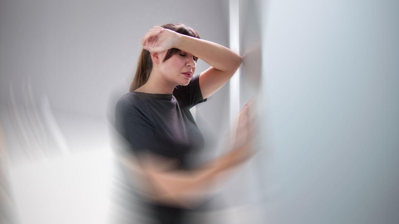 Imagem de uma mulher com tontura apoiada na parede