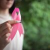 Foto mostra mulher segurando um laço rosa.