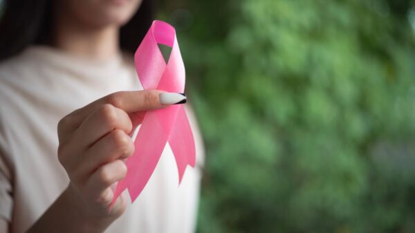 Foto mostra mulher segurando um laço rosa.