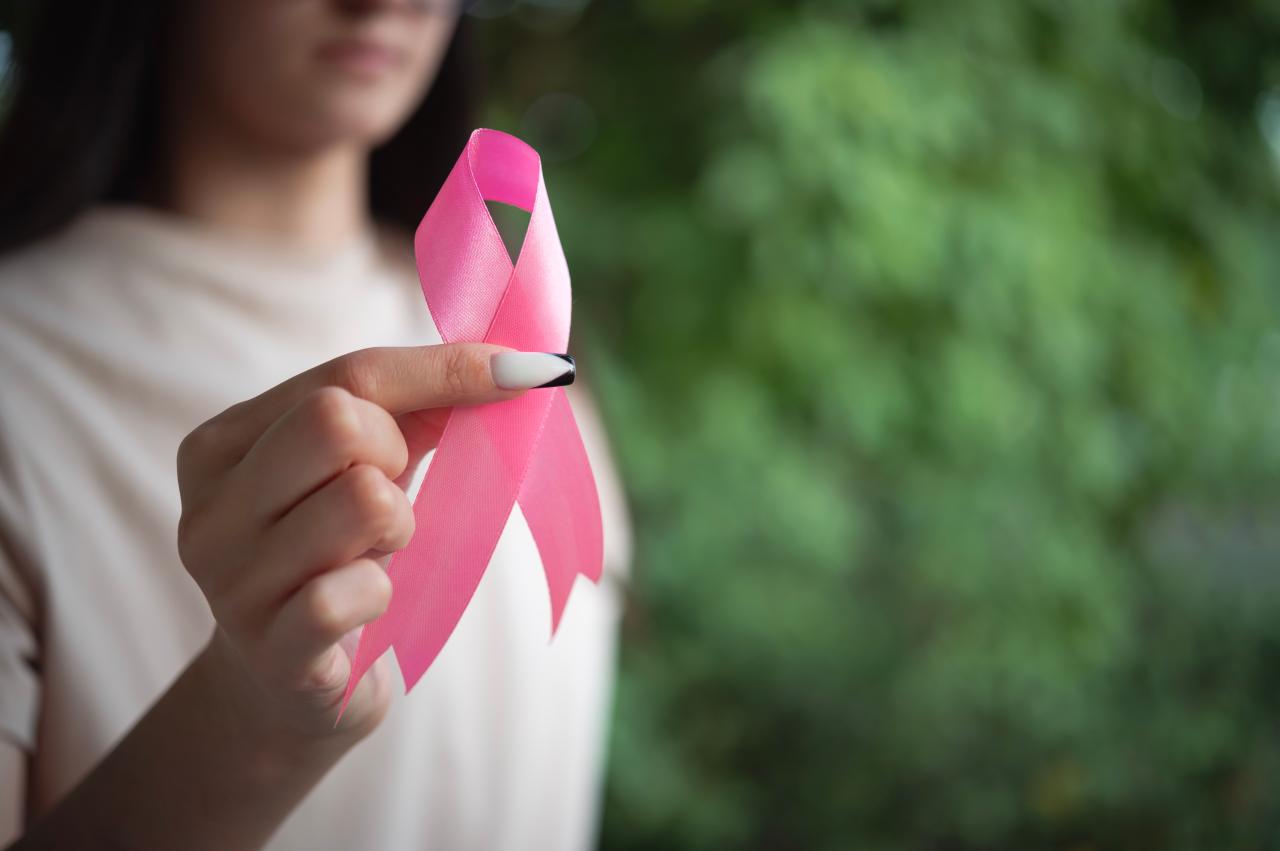 Foto mostra mulher segurando um laço rosa.