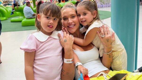 Foto mostra Virginia sentada na cadeira com as filhas ao lado.