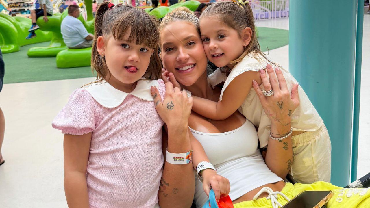 Foto mostra Virginia sentada na cadeira com as filhas ao lado.