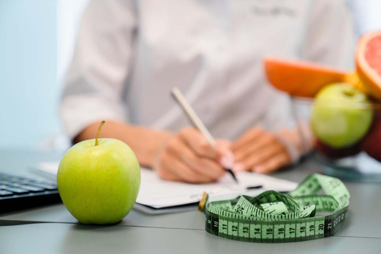 Mesa de nutricionista com maça verde e uma fita métrica.