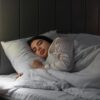 Mulher dormindo em cama com lençol branco.