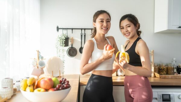 Duas mulheres na cozinha com frutas nas mãos e no cesto da bancada da cozinha.