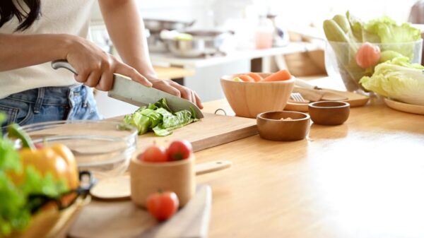 Pessoa cortando alimentos em uma tábua em cima da bancada da cozinha.