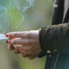 Foto mostra uma mão com esmalte nas unhas segurando um cigarro.