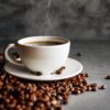 Xícara de café cheia com grãos torrados ao lado em cima de uma mesa.