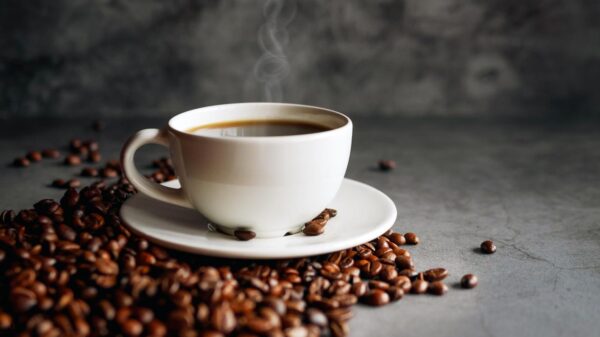 Xícara de café cheia com grãos torrados ao lado em cima de uma mesa.