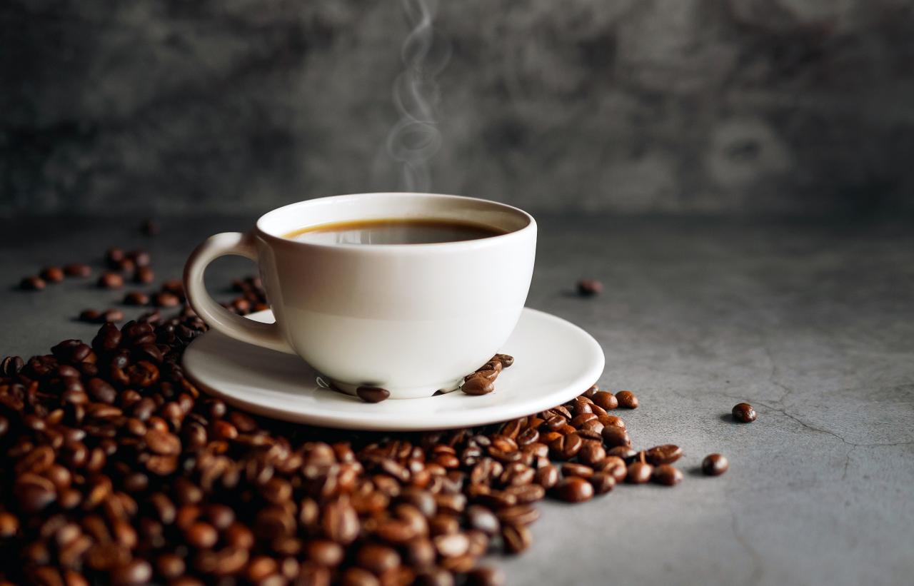 Xícara de café cheia com grãos torrados ao lado em cima de uma mesa.