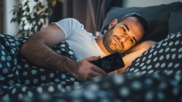 Homem deitado na cama com o celular na mão com a tela brilhando o rosto dele.