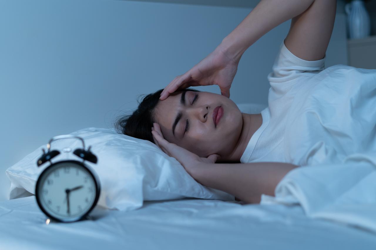 Mulher deitada na cama com rosto de quem está dormindo mal.